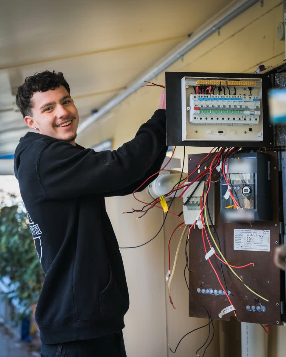 A JJC electrician smiling beside a rewired switchboard and meter panel
