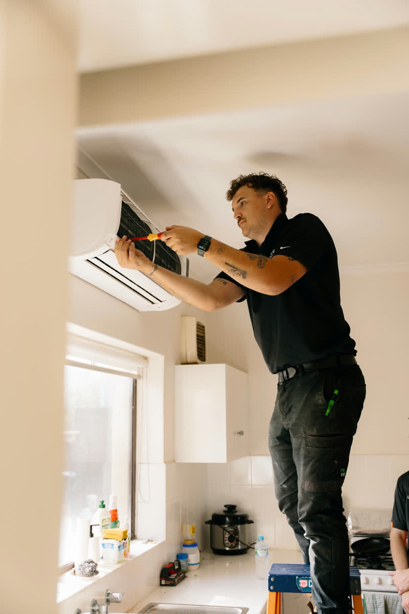 A JJC electrician on a ladder installing a split system indoors